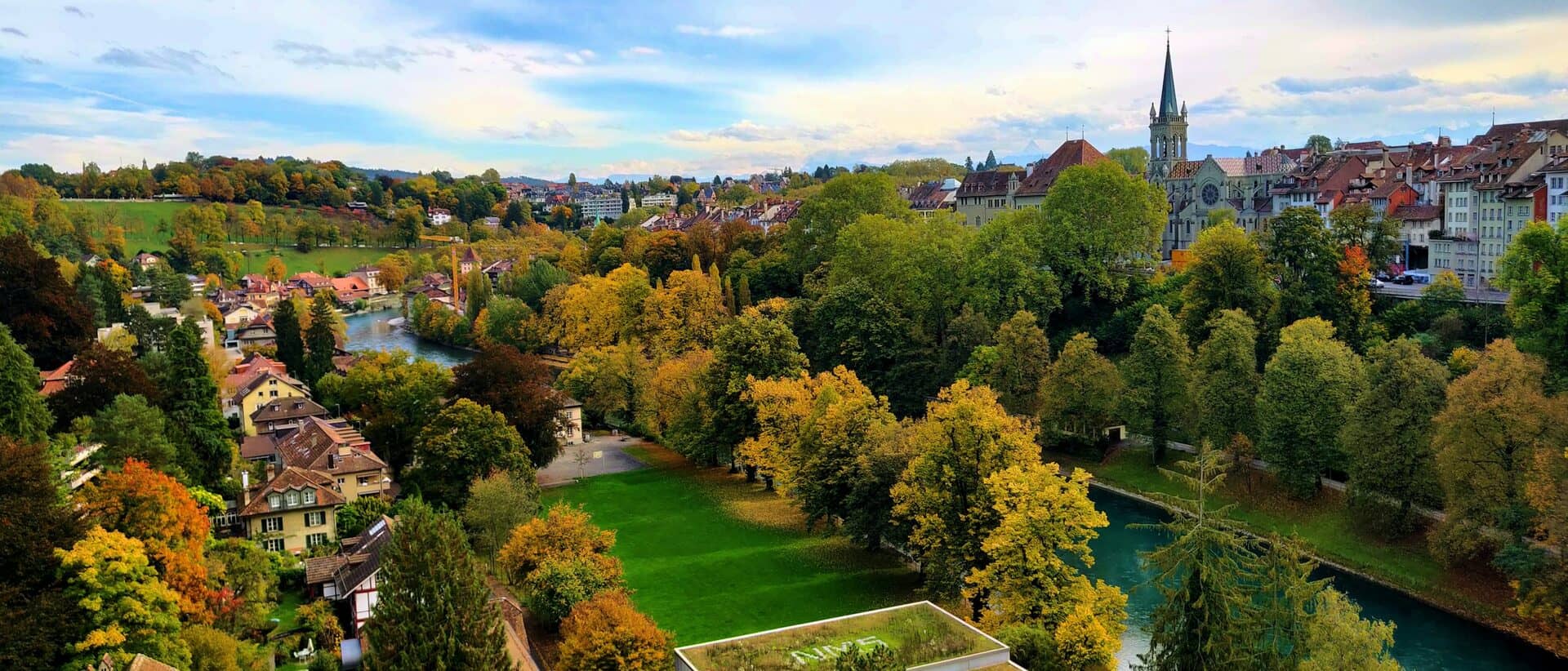La vieille ville de Berne et l’Aar — toits, arbres d’automne et le clocher de la collégiale au-dessus de la rivière.