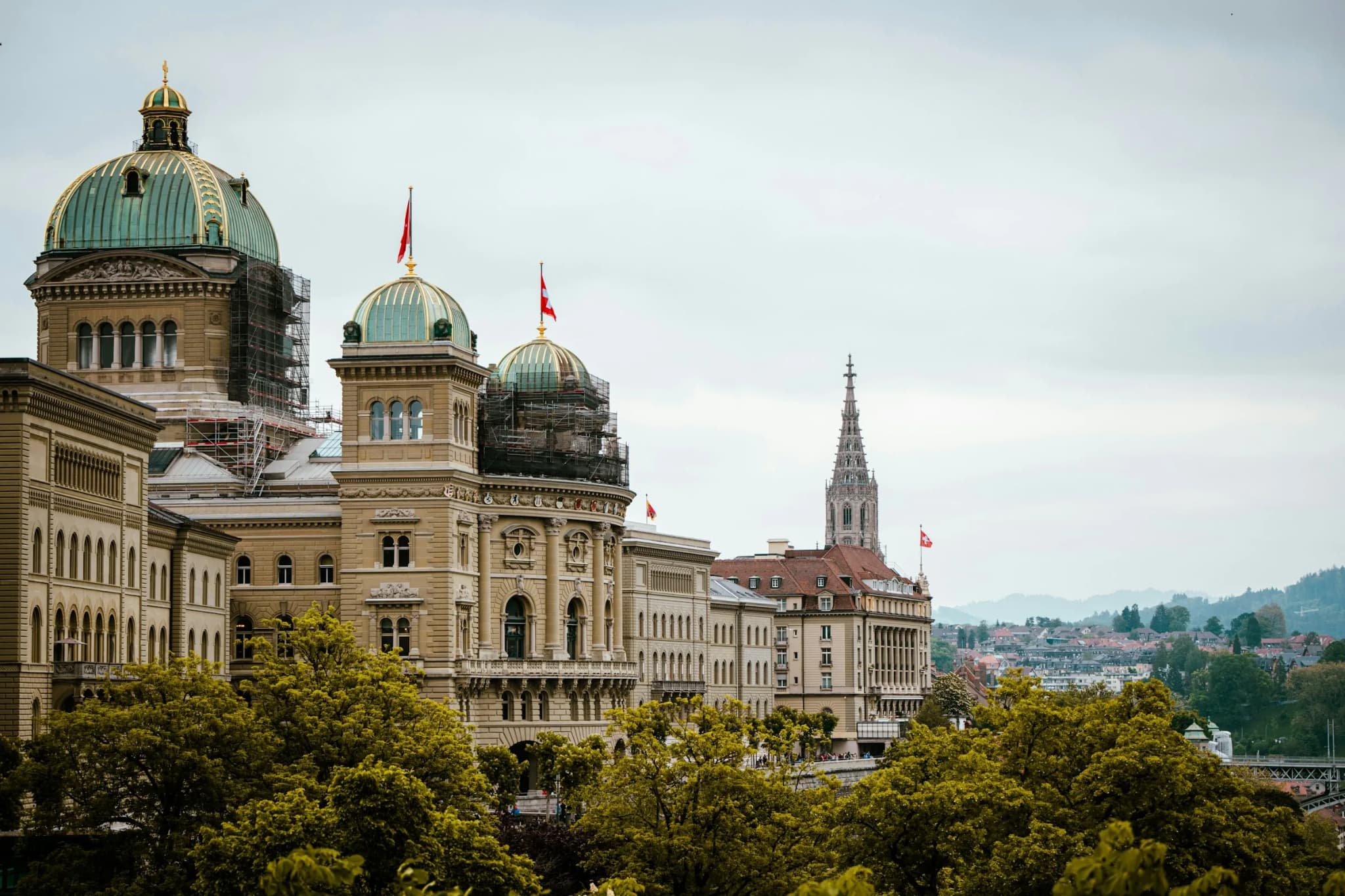 Bundeshaus in Bern mit Schweizer Fahnen, dahinter der Turm des Berner Münsters